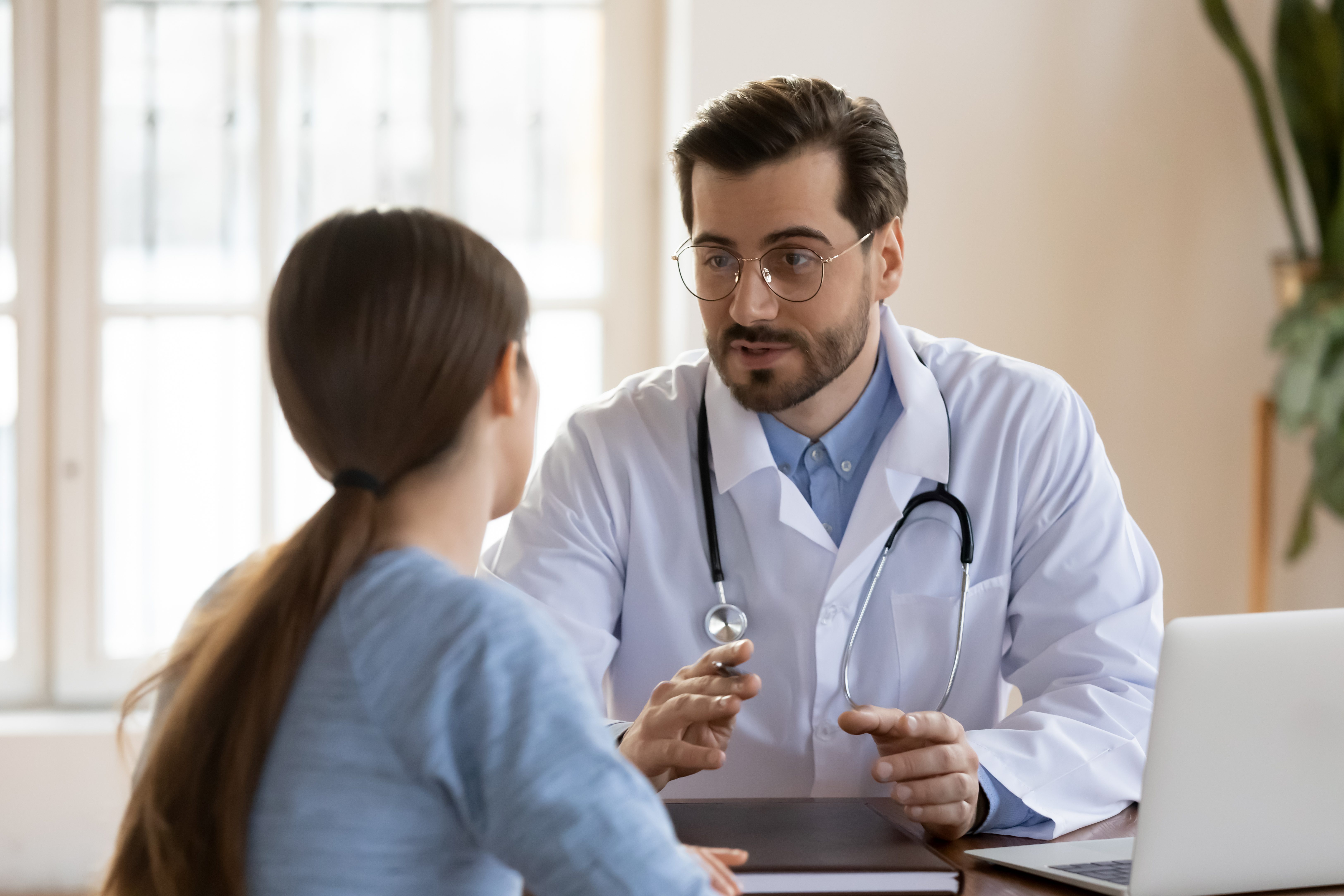 Serious Caucasian male doctor in white medical uniform talk discuss results or symptoms with female patient, man GP or physician consult woman client give recommendation at meeting in hospital