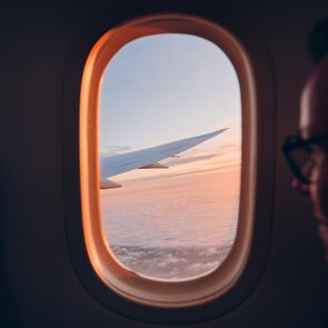 Man looking through a vindow of airplane; clouds and the plane's wing can be seen out the window