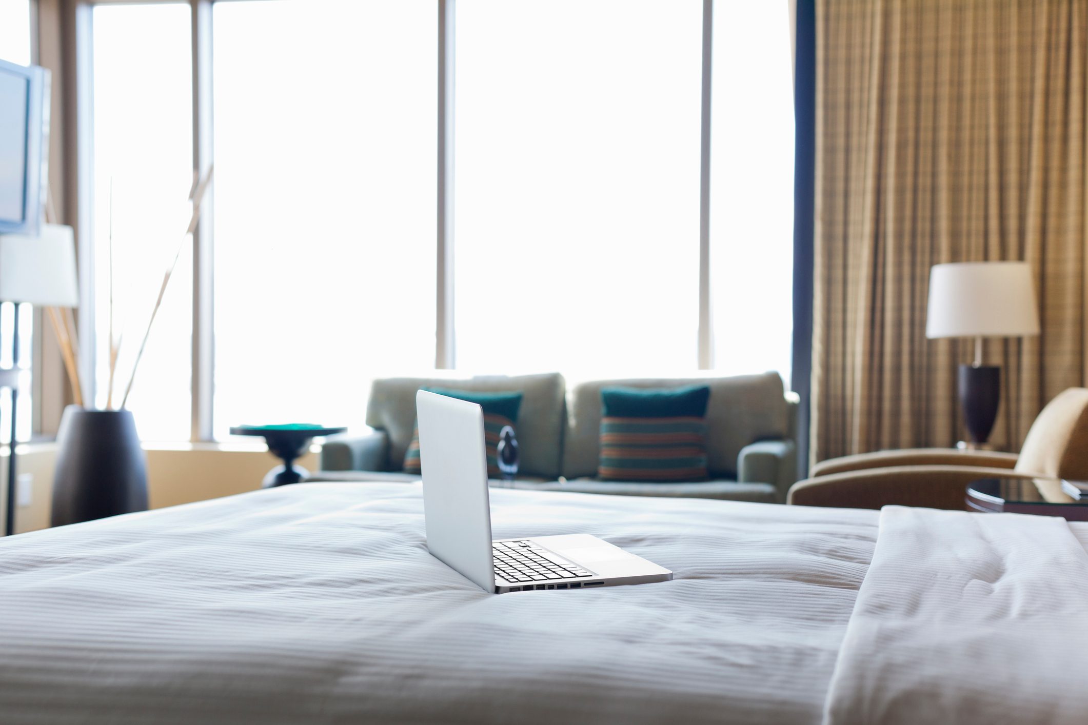 Laptop computer on bed in empty hotel room.