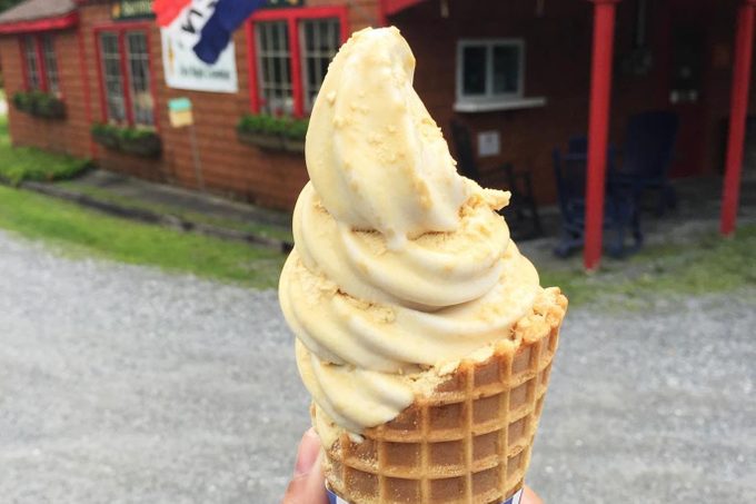 hand holding Maple ice cream in a cone in front of an ice cream stand