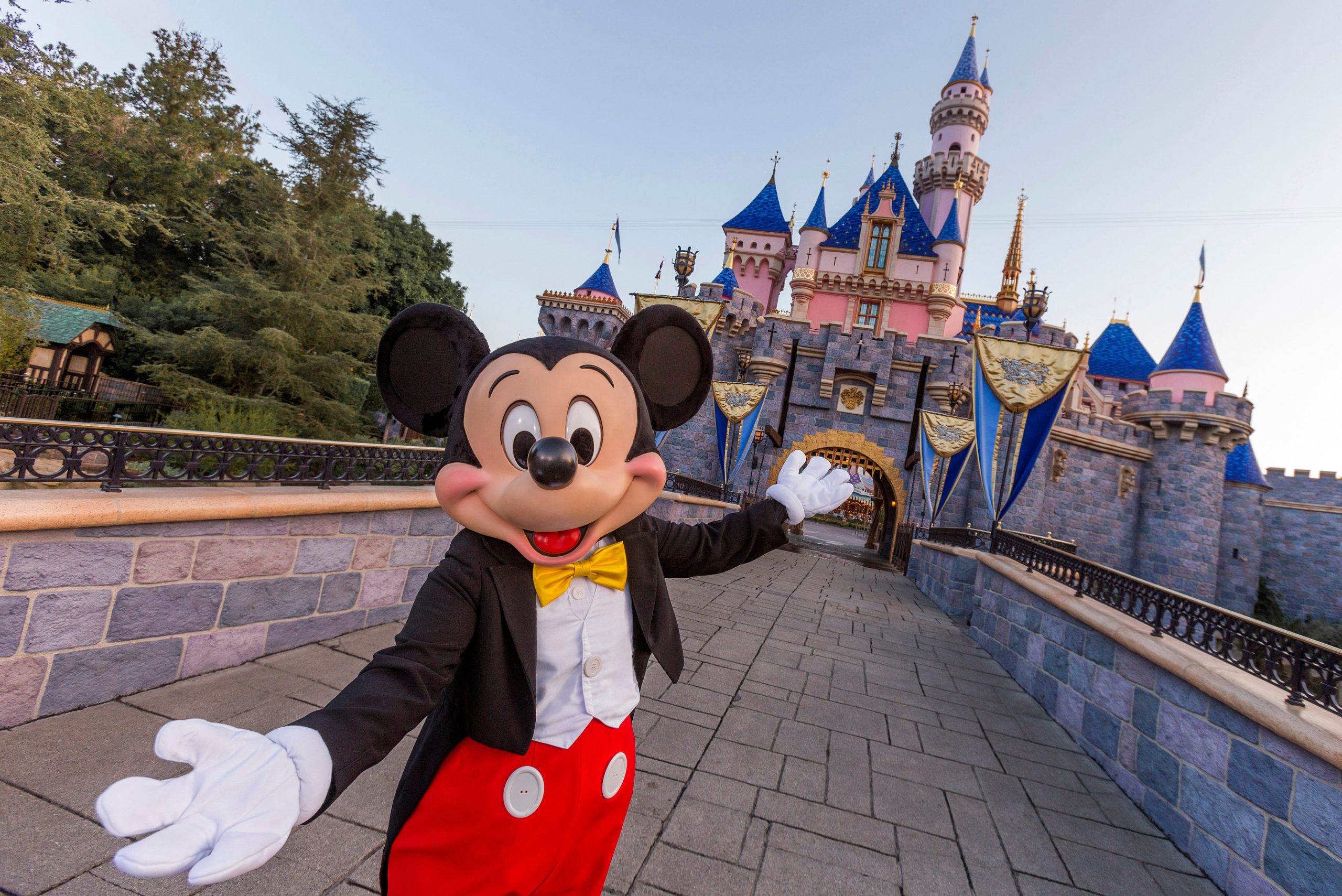 Mickey Mouse smiling with arms open in front of Disneyland castle