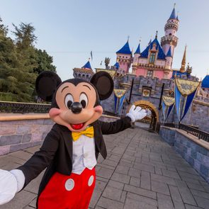 Mickey Mouse smiling with arms open in front of Disneyland castle