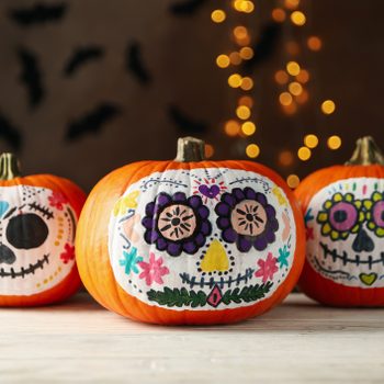 Pumpkins with catrina skull makeup on brown background with blurred lights