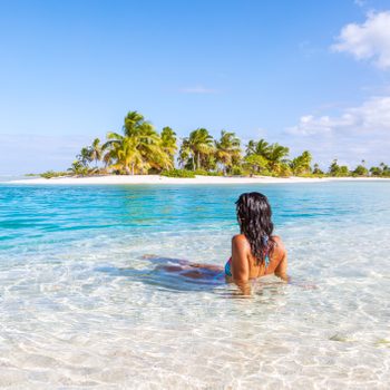 Woman sitting in a blue lagoon in front of tropical island