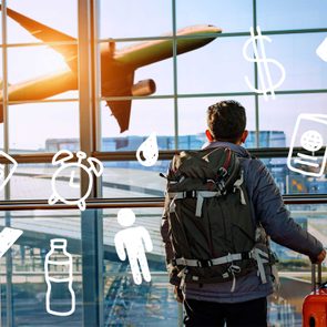 Male tourist is standing in airport and looking at airplane flight through window.