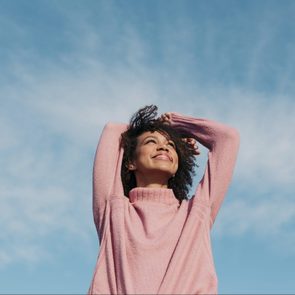Portrait Of Happy Young Woman in pink sweater Enjoying Sunlight and blue sky