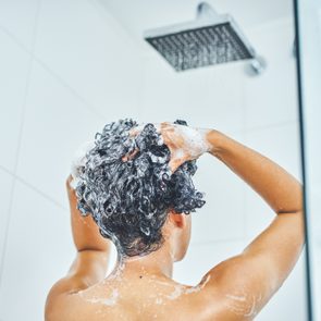 person from behind washing their hair with shampoo in the shower at home