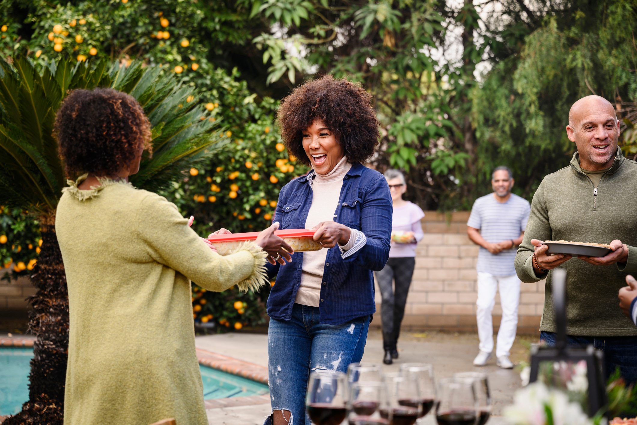 smiling friends holding prepared food for a potluck dinner