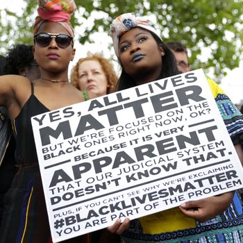 Two women hold a placard with the slogan "Yes, all lives matter" as people gather in protest