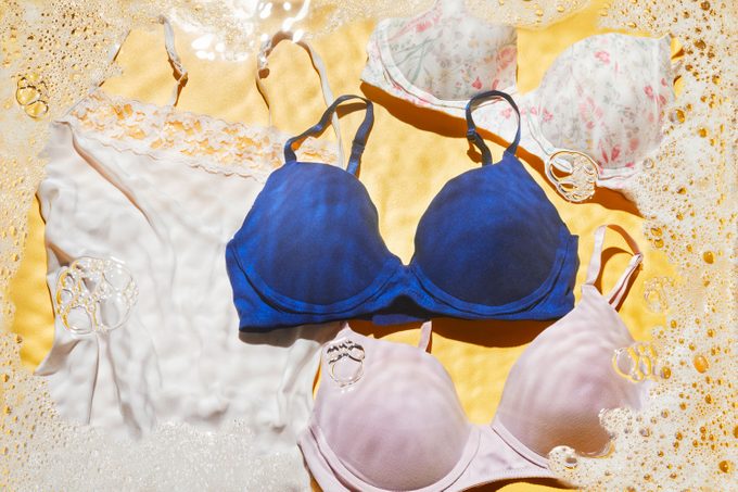 Camisole and three bras on yellow background with soap bubbles and water effect