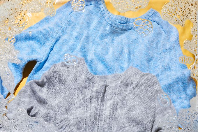 A light blue sweater and a light gray sweater on yellow background with soap bubbles and water effect