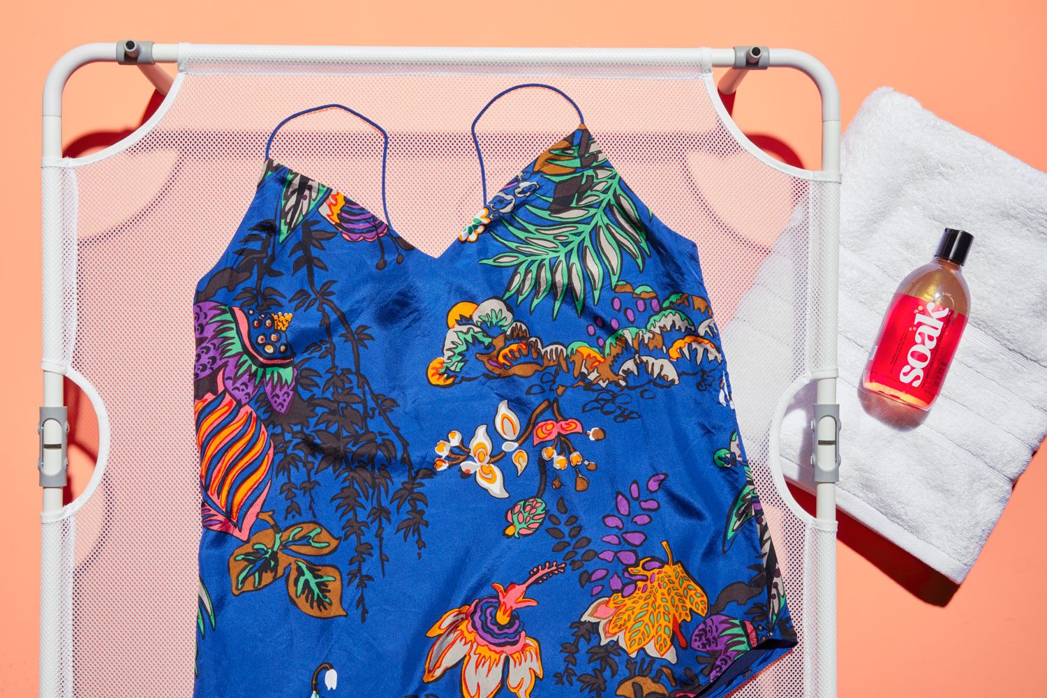 Silk tank top with hand washing supplies on orange background. the garment is laid on a tabletop mesh drying rack and a towel and no-rinse detergent are nearby