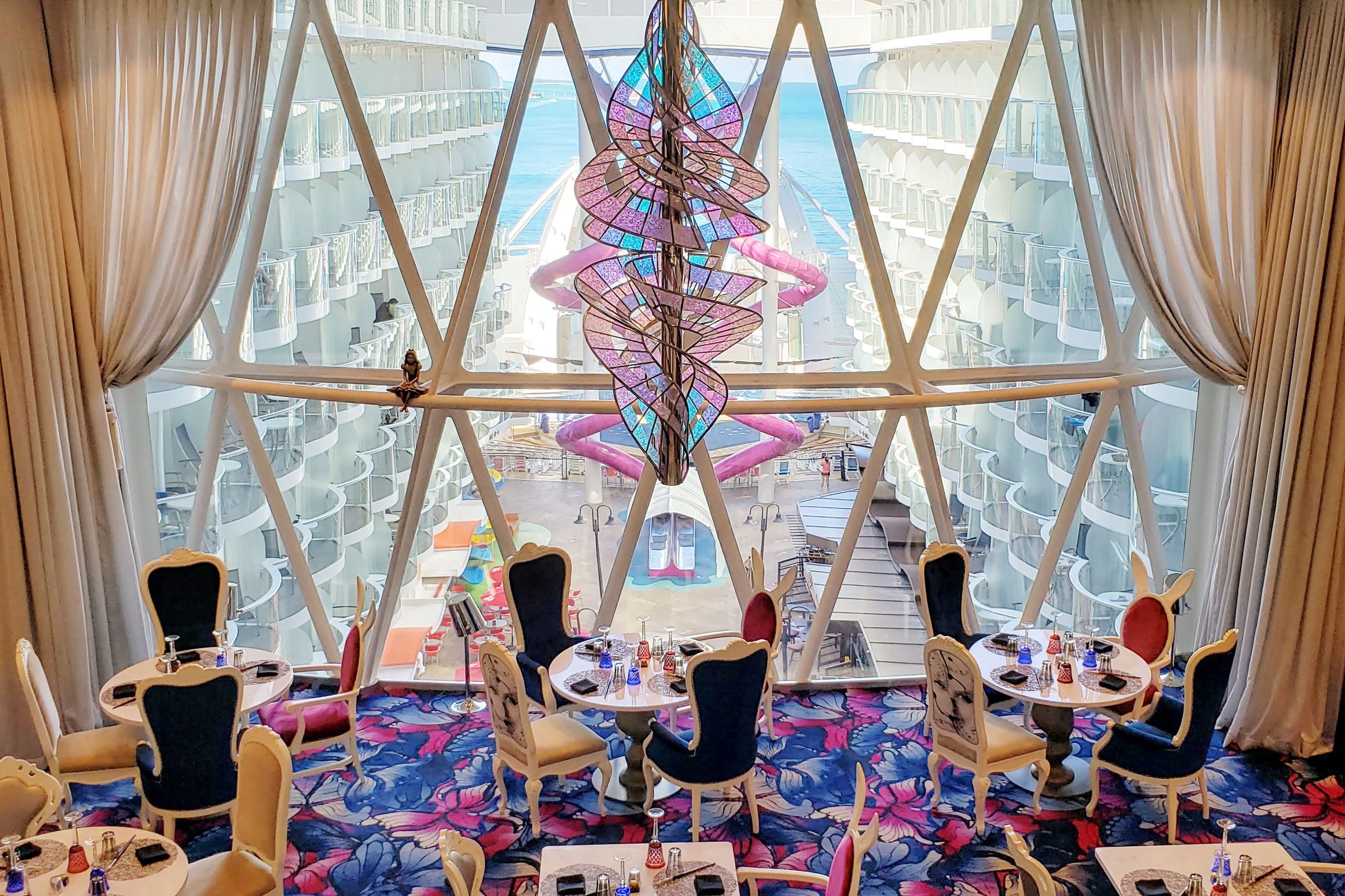 Cruiseship Dining Room and chanelier in foreground with large windows overlooking another area of the ship in the background