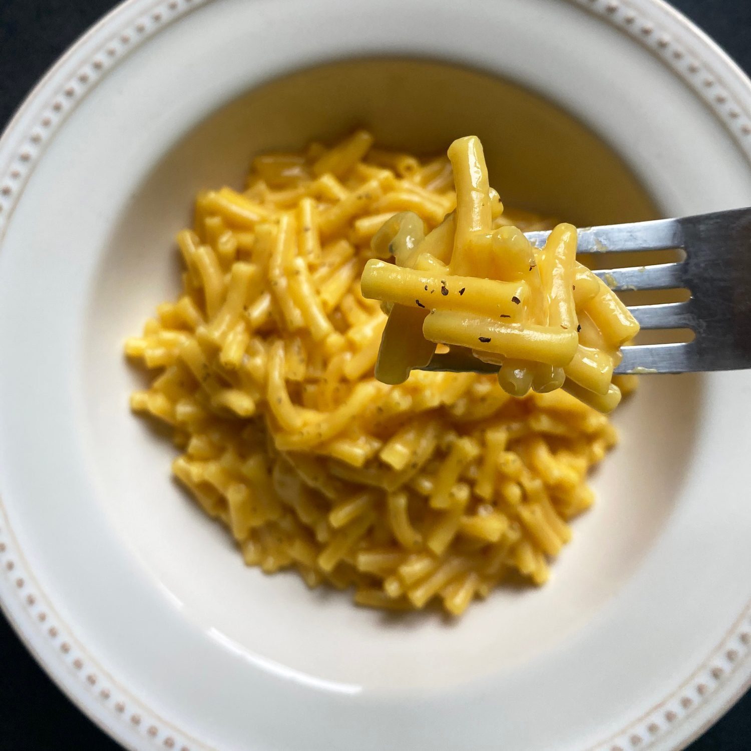 Tik Tok Mac And Cheese on the end of a fork in the foreground, in a white bowl in the background