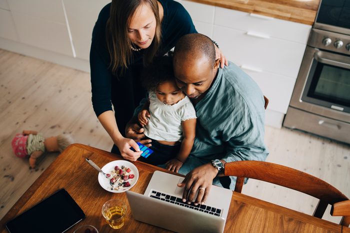 High angle view of parents with daughter shopping online on laptop at dining room