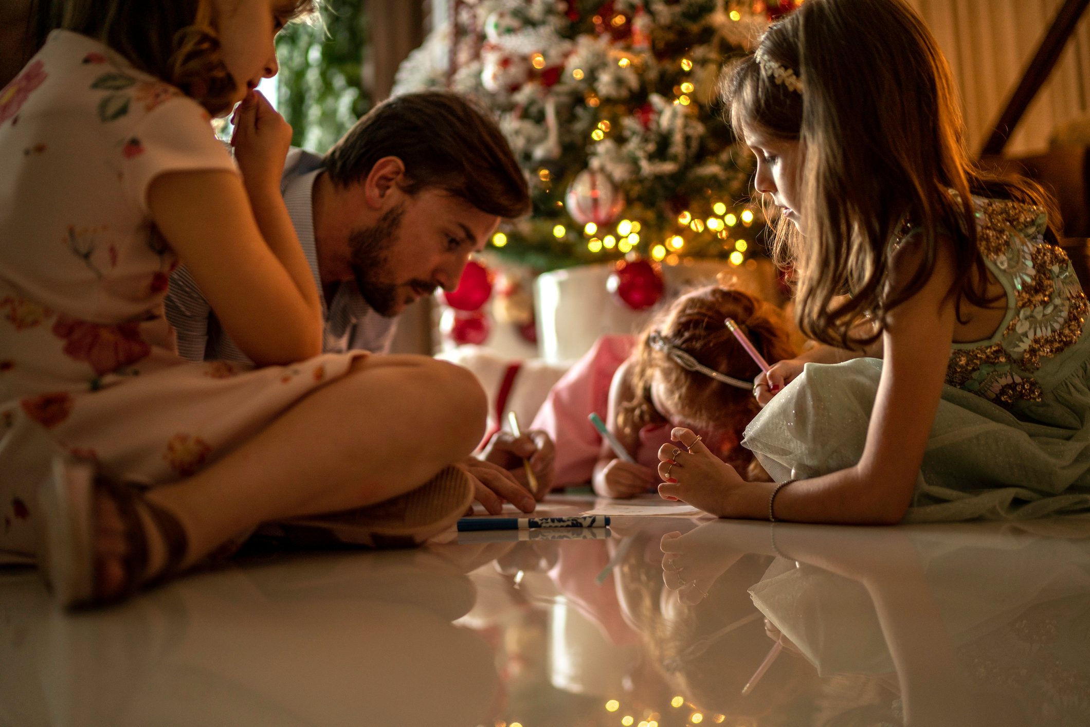 family writing letters to santa near the christmas tree at home