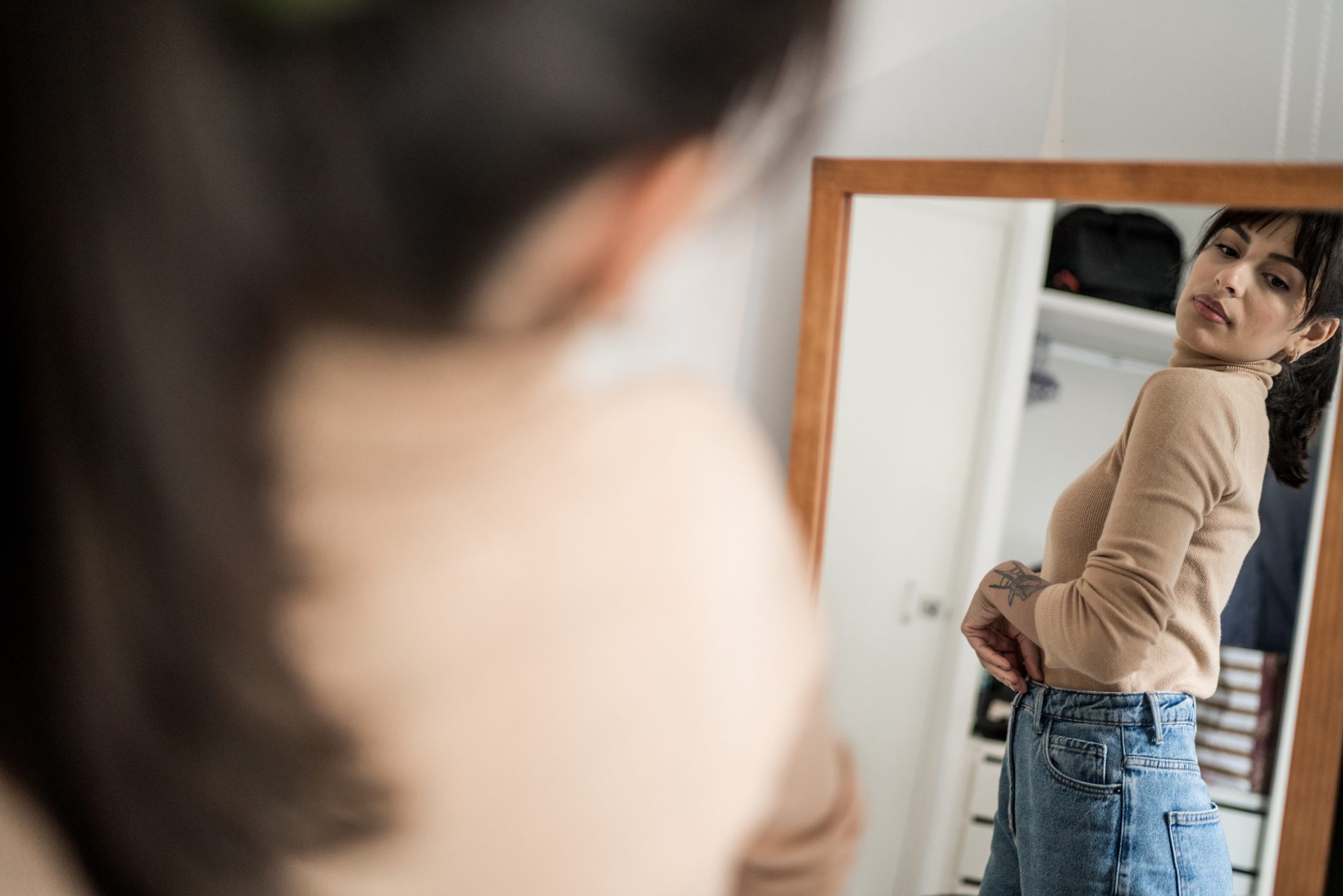 Young woman getting dressed in front of a mirror at home