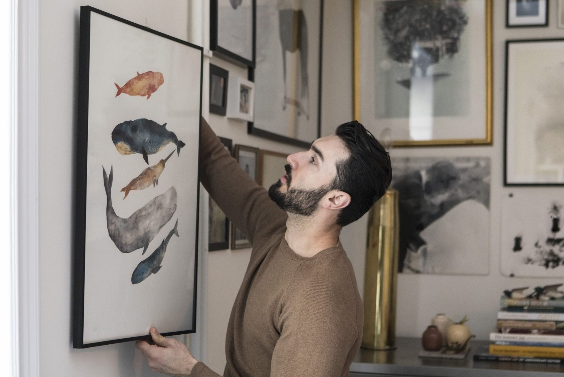 Young man hanging painting on wall at home