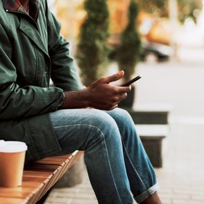 close up of man sitting on bench looking at smartphone