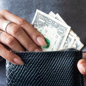 close up on hands pulling a few dollar bills out of a black wallet for a tip