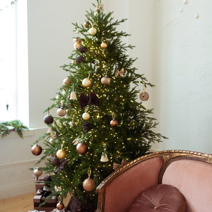 Pastel maroon sofa near e beautiful decorated Christmas tree. Balls ornaments garlands in rose gold brown style decoration on Christmas tree.