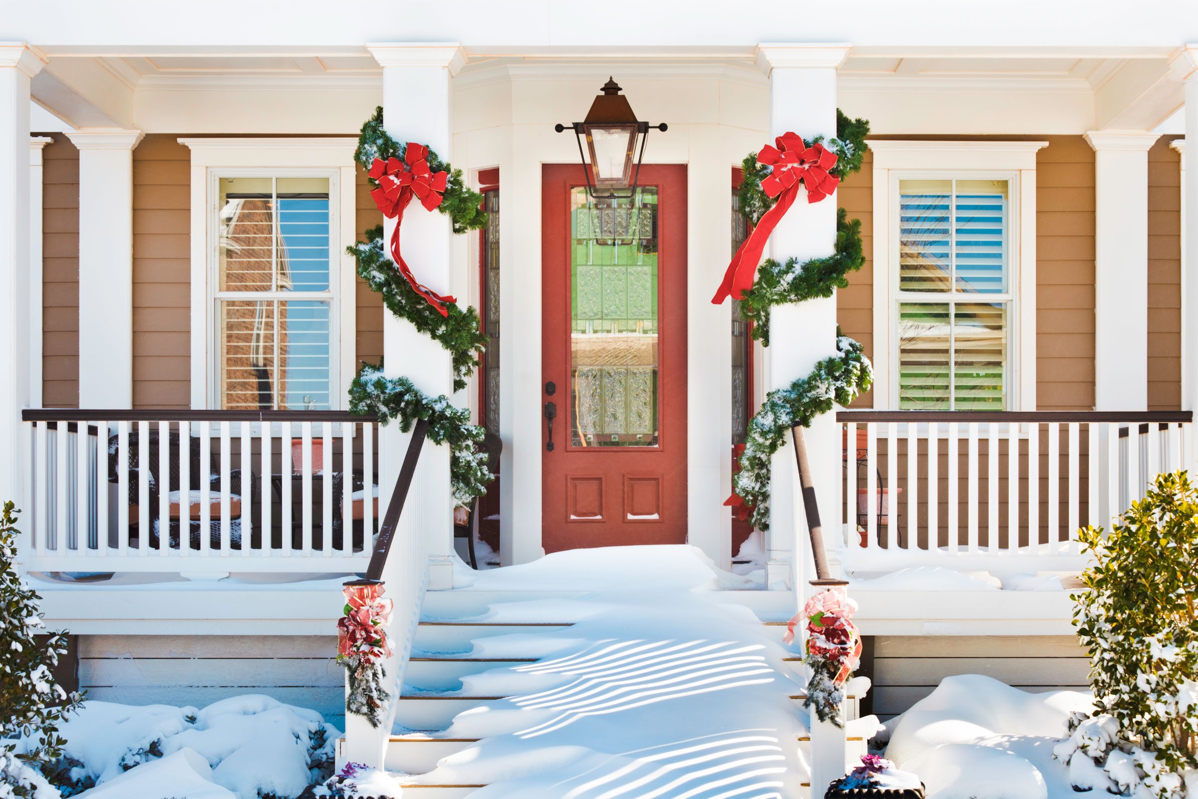 inviting doorway with snow on porch stairs and railing and christmas garland wrapped around two posts