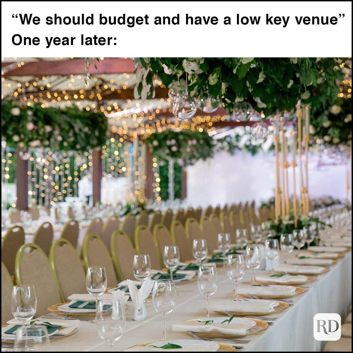 Lush floral garland with white roses hangs over the stylishly served white tables on the spacious terrace. Wedding reception is illuminated with electric garlands, green garden is on the background.