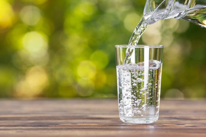 Water,from,jug,pouring,into,glass,on,wooden,table,outdoors