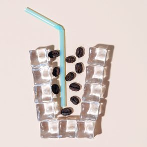 flat lay of coffee beans and a blue straw inside a cup shaped outline made with ice cubes; cold brew coffee concept