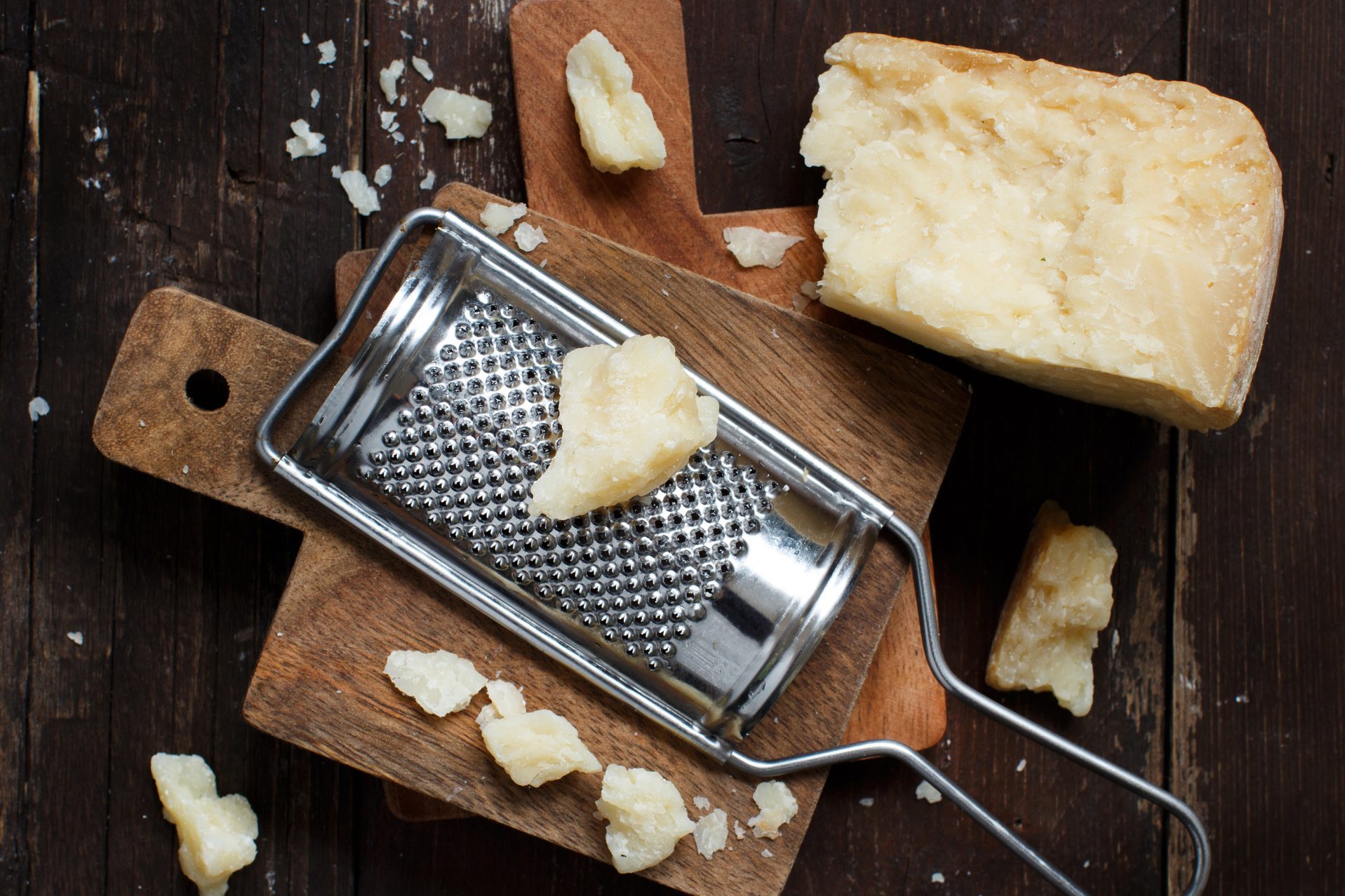 Aged parmesan cheese and grater on a cutting board on a dark background