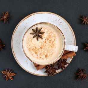 overhead view of chai tea in a white mug on a saucer on a dark slate background surrounded by spices