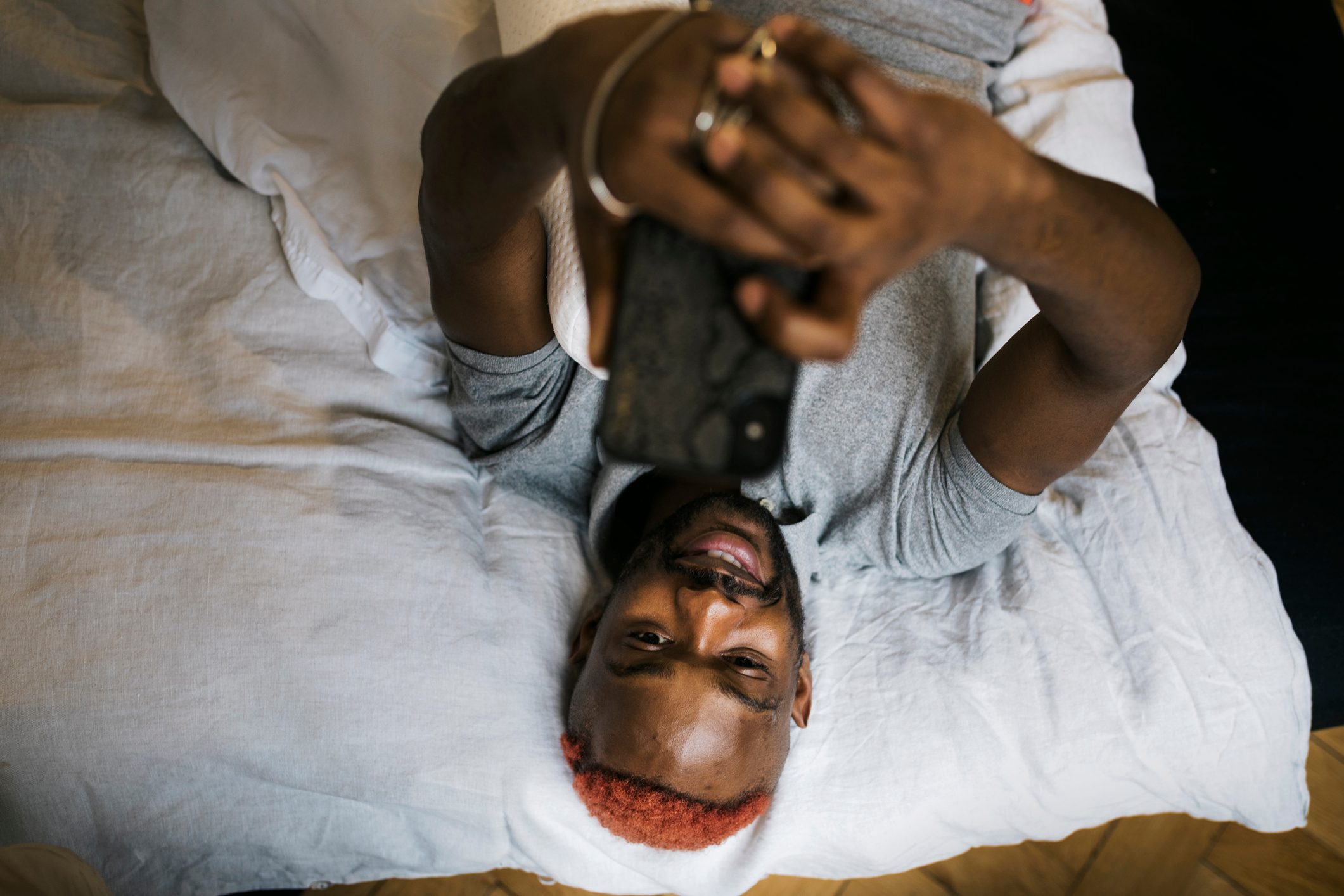 Man Smiling While Laying On Bed Messaging Using Smartphone