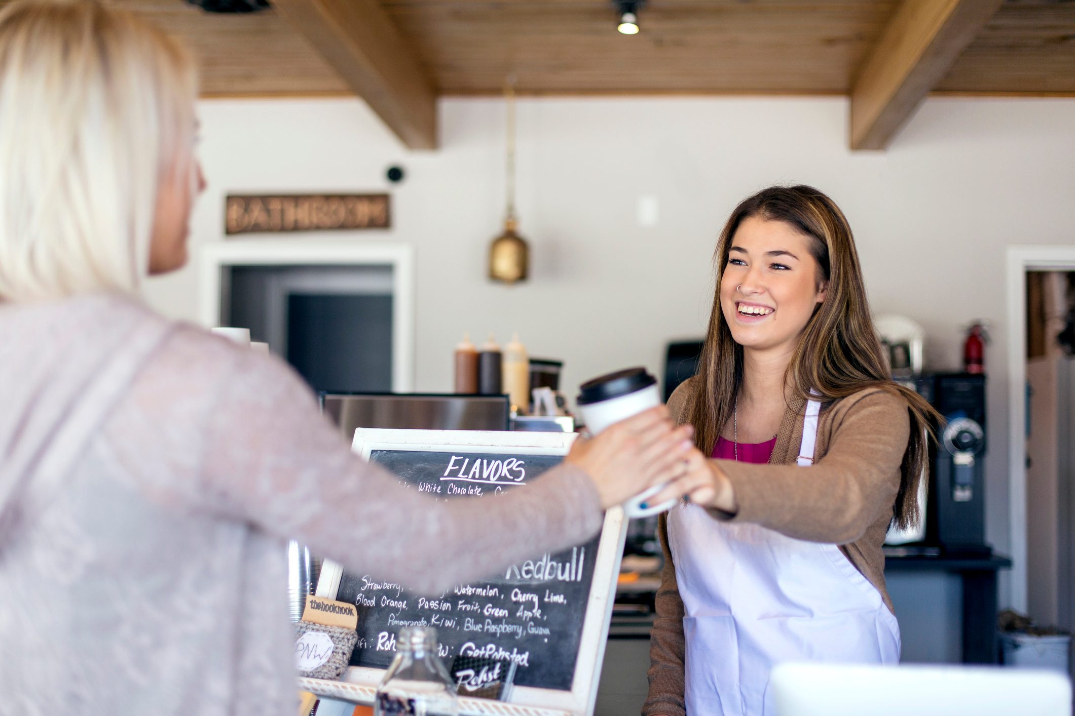Attractive young female barista handing coffee to a customer