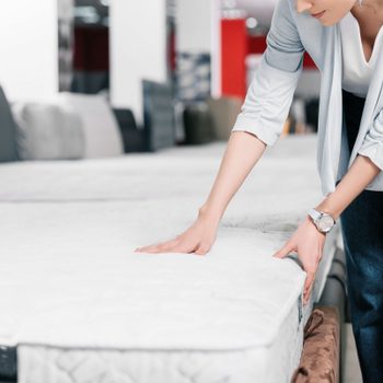 partial view of woman touching orthopedic mattress in furniture shop