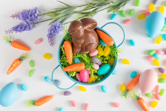 Close-up of Easter basket with chocolate bunny, mini carrots, and candy eggs on white background