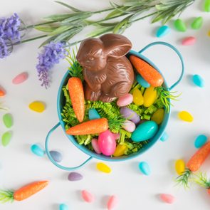 Close-up of Easter basket with chocolate bunny, mini carrots, and candy eggs on white background