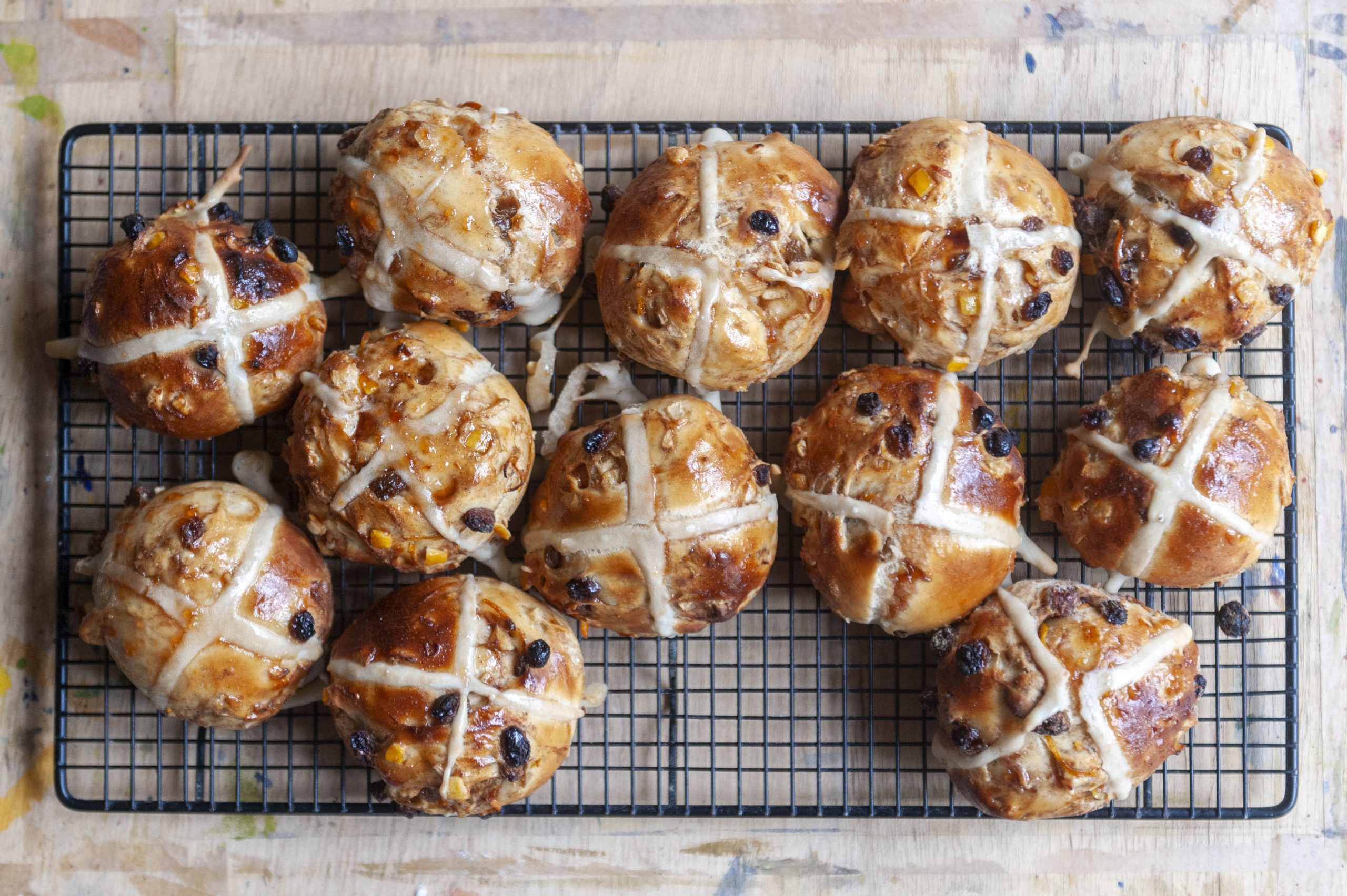 A close-up aerial view of freshly baked hot cross buns on a wire rack with a wooden surface beneath.