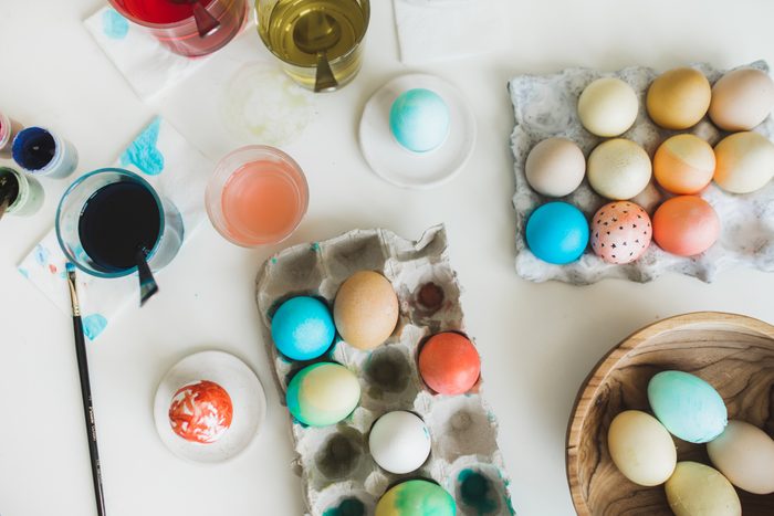 Close up of coloring easter eggs with colors and brush. Tools for painting eggs for easter, eggs box, plate, brushes and paints on the table, top view.