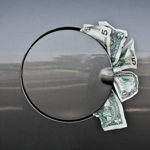 close up of car's gas cover with one and five dollars bills sticking out