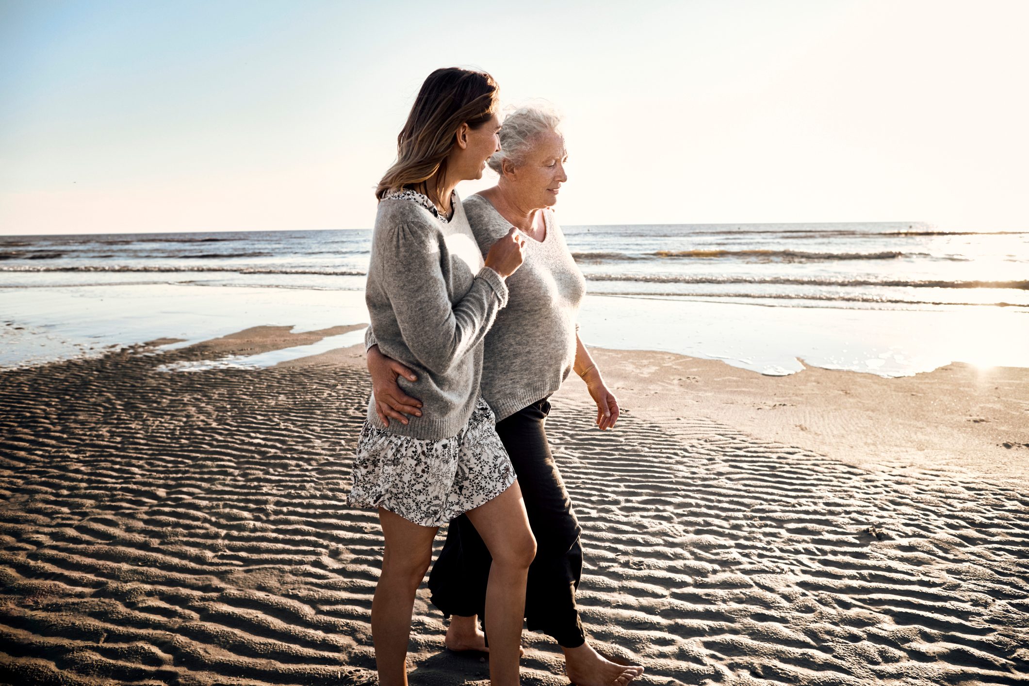 Mother and daughter strolling on the beach at sunset