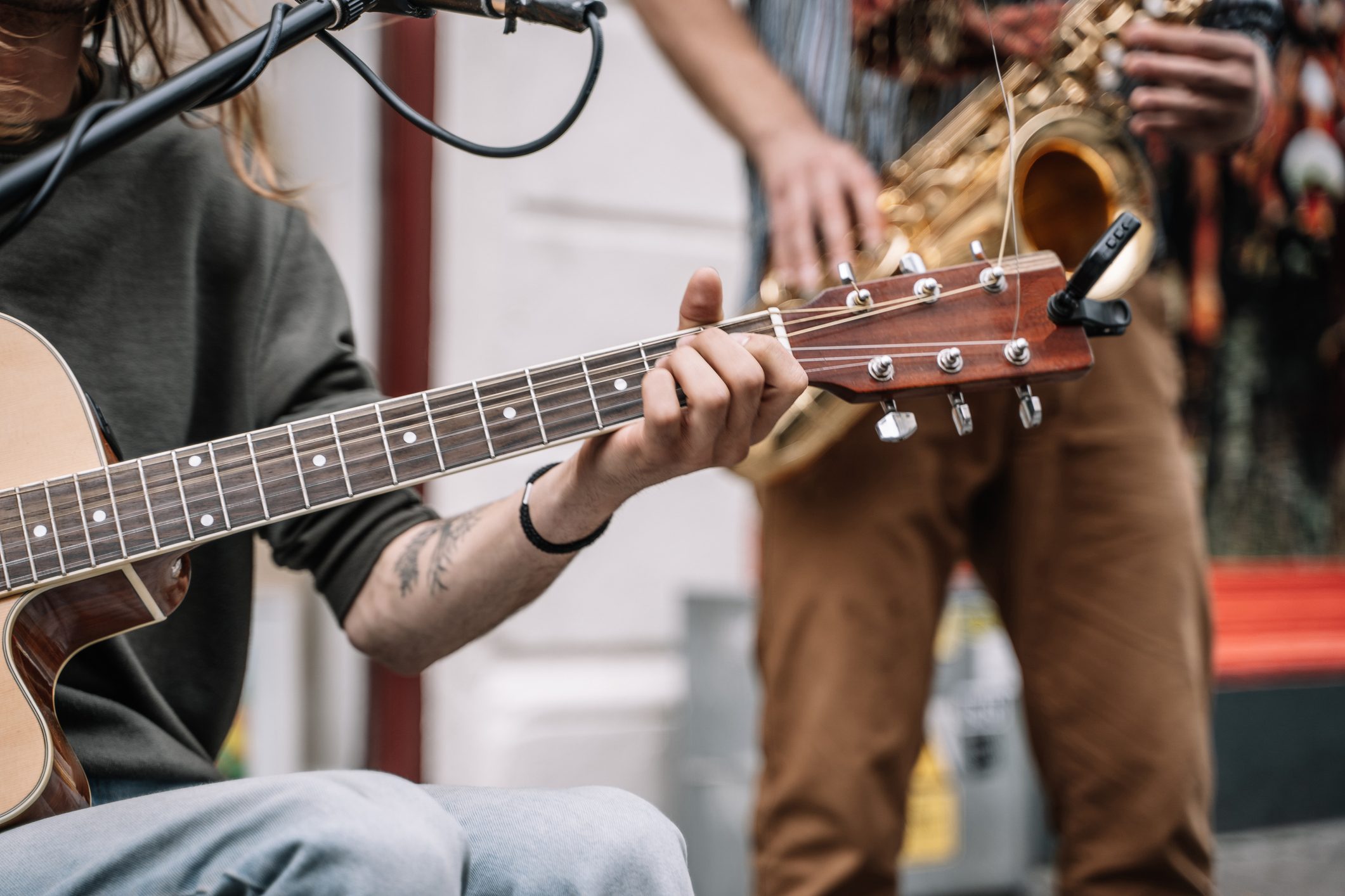 Musician playing guitar in the middle of the street in front of a microphone and with a saxophonist