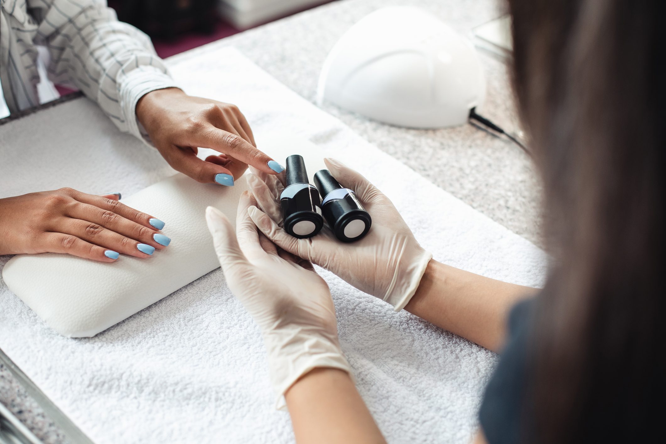 Professional nail care. African american woman client chooses gel polish in hands of master in rubber gloves in modern salon with equipment for manicure