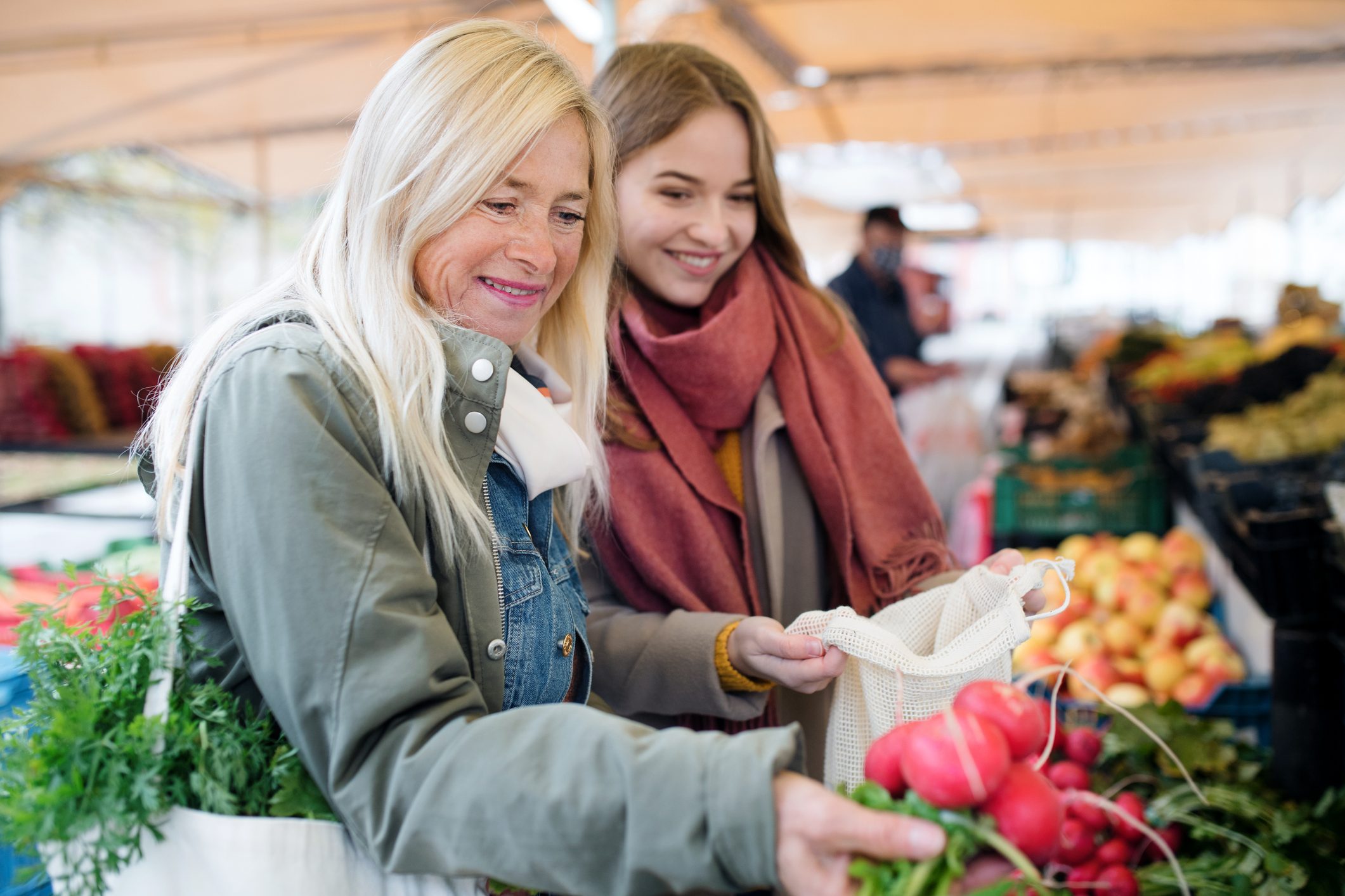 Senior and young woman buying vegetables on outdoor martket, talking.