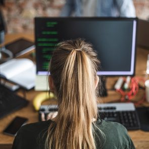 Blond female programmer coding over computer in startup company