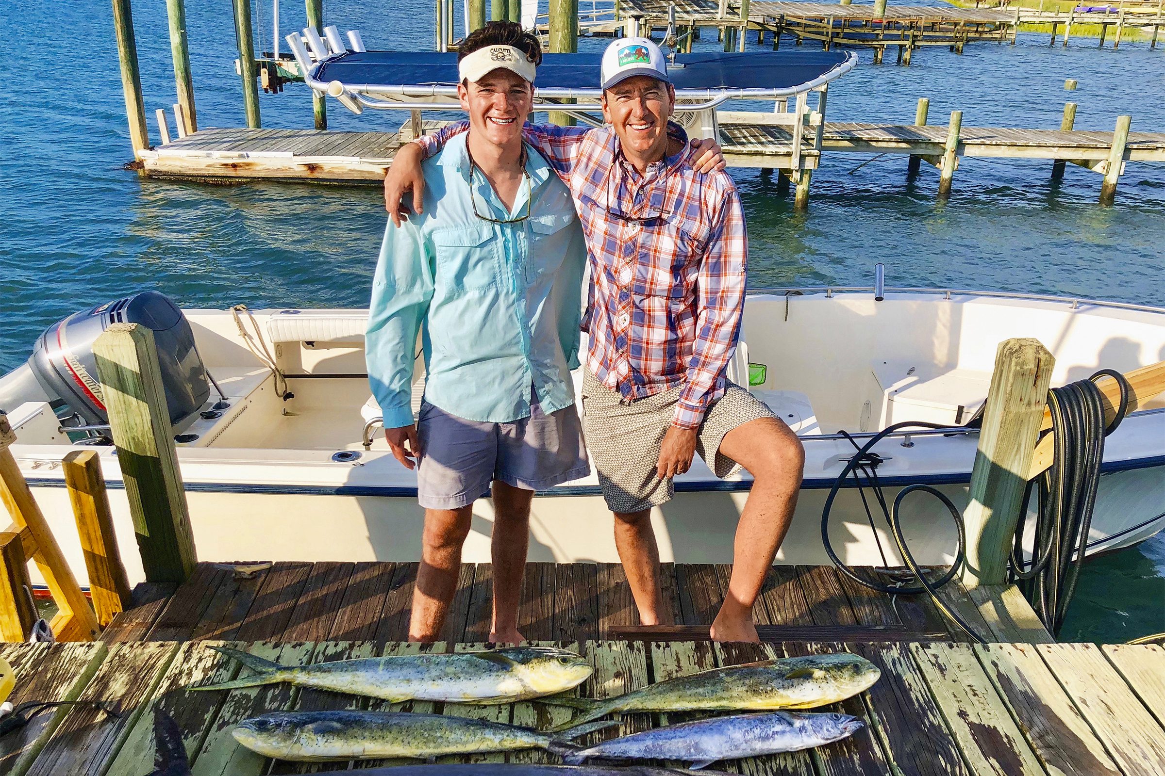 A fisherman and his son standing on a dock with fish they caught