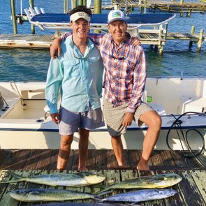 A fisherman and his son standing on a dock with fish they caught