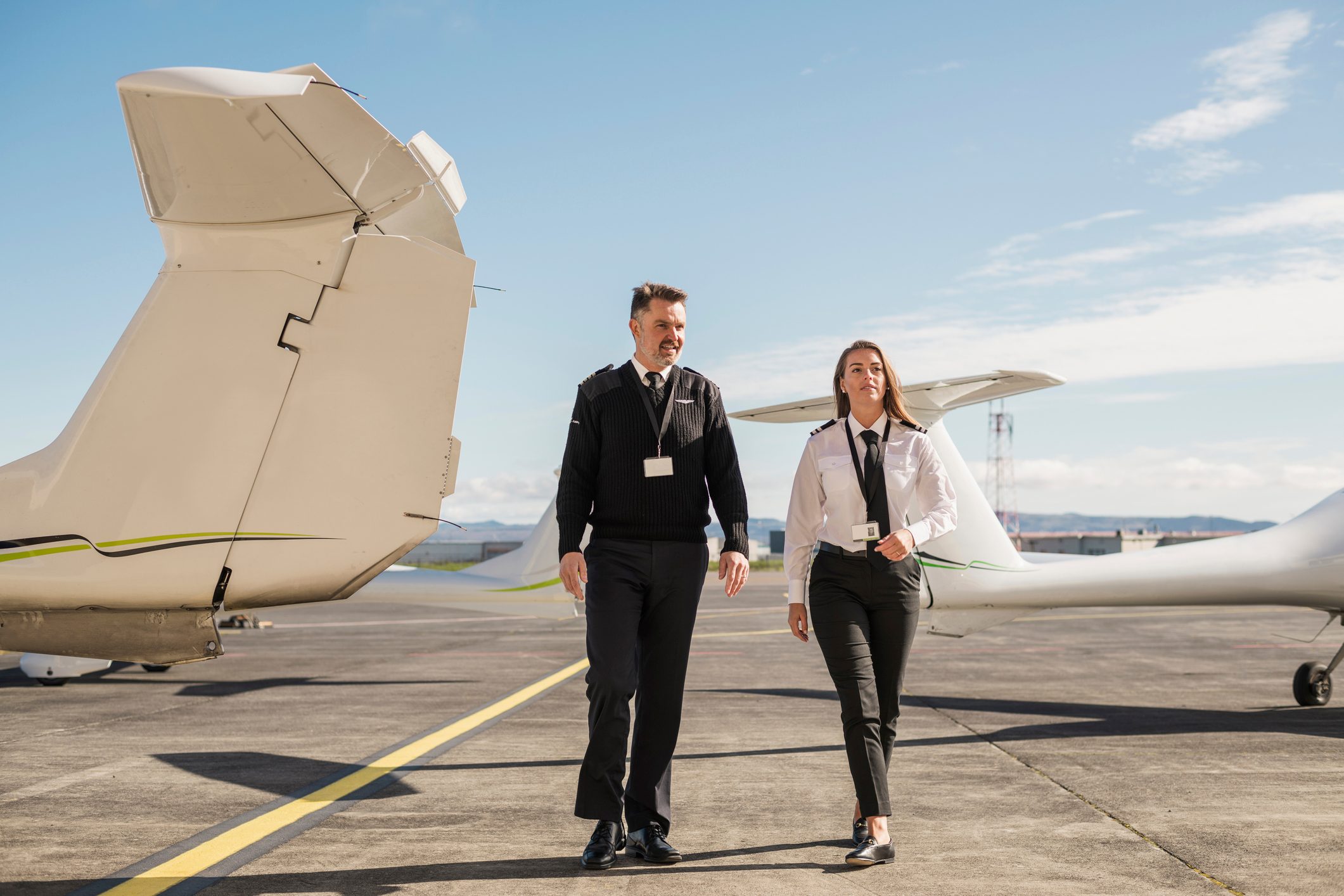 Pilots talking while walking on airport runway against blue sky during sunny day