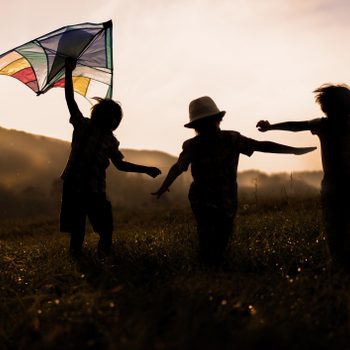 three happy children flying kites at sunset