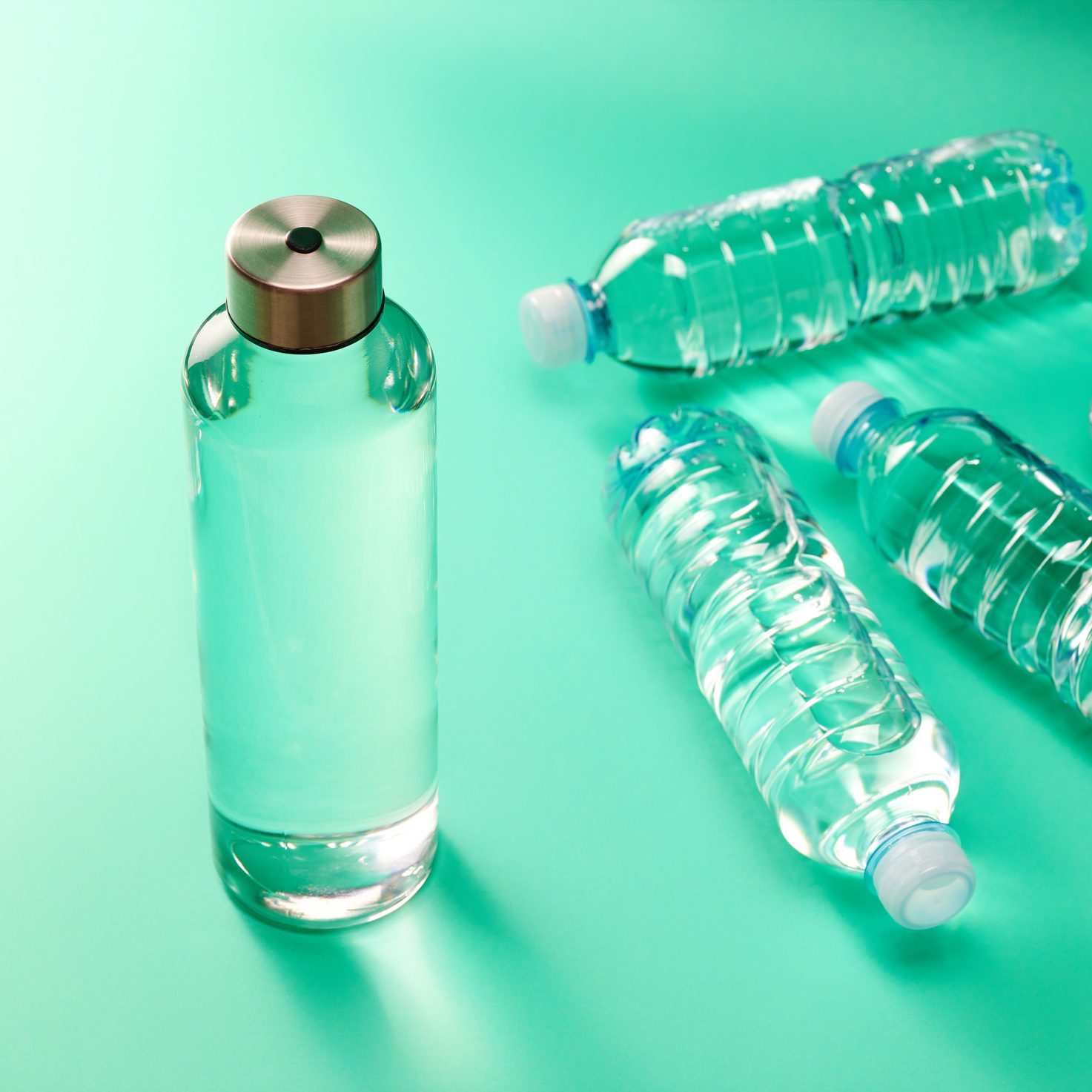 Refillable drinking water bottle and single use plastic bottle on mint green background