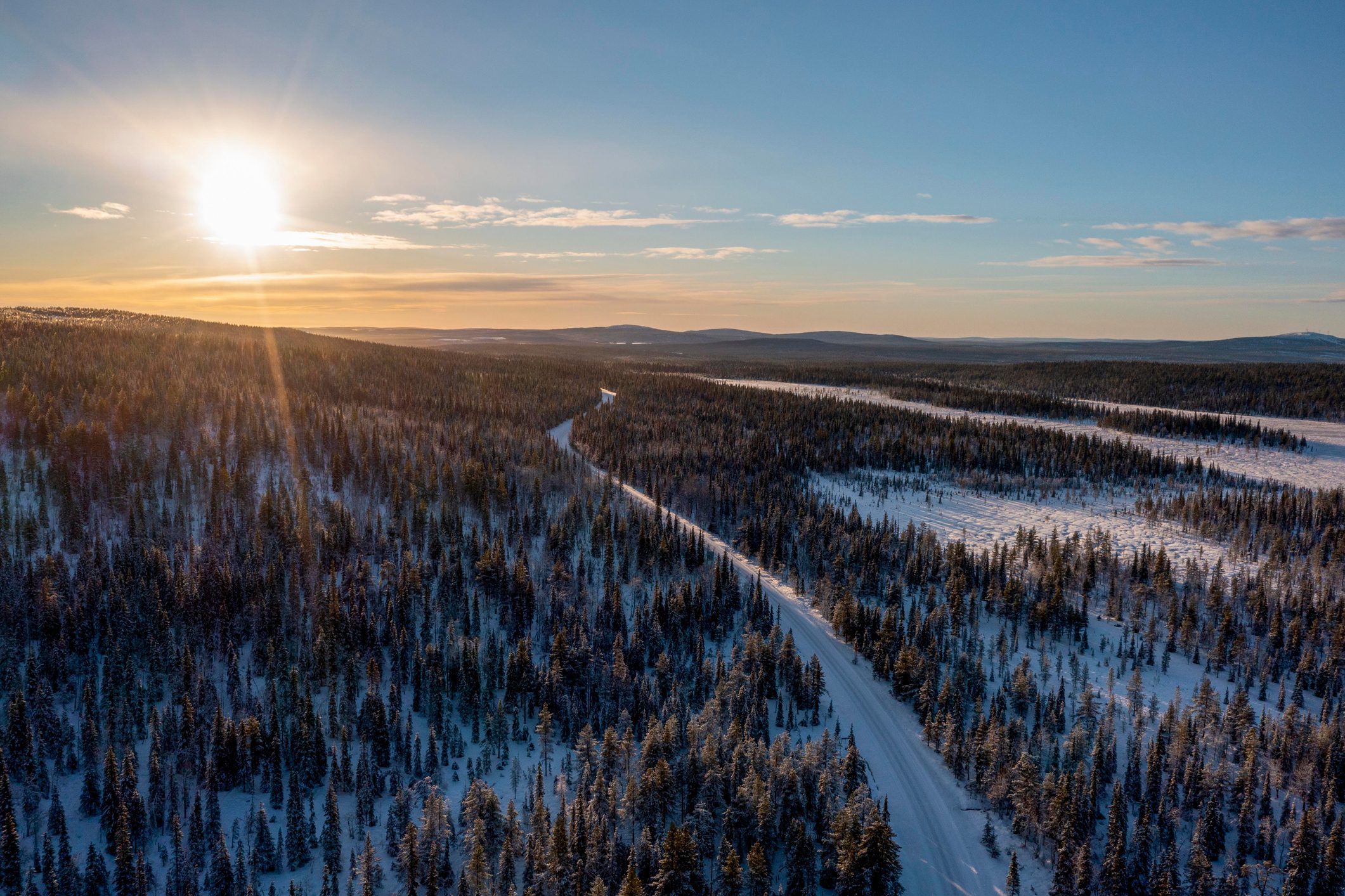 Snowy forest road with setting sun in Lapland, Finland